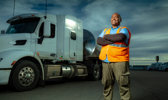 a truck driver wearing a hi-vis vest posing in front of her trailer truck